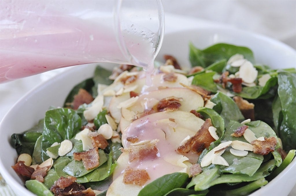 pouring dressing over spinach apple salad