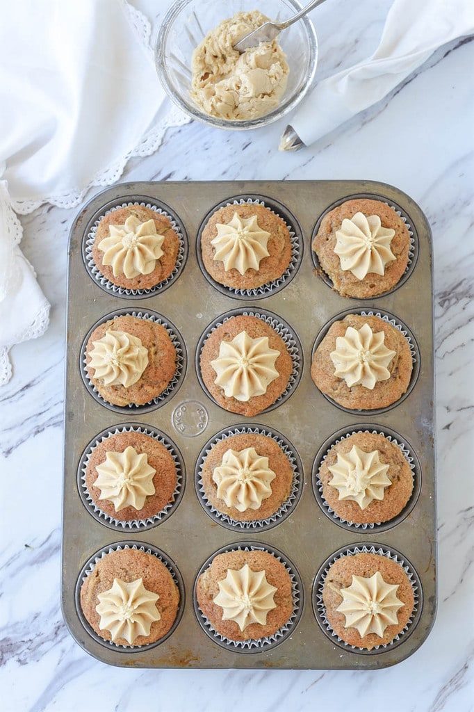 12 zucchini cupcakes with caramel frosting in a muffin tin