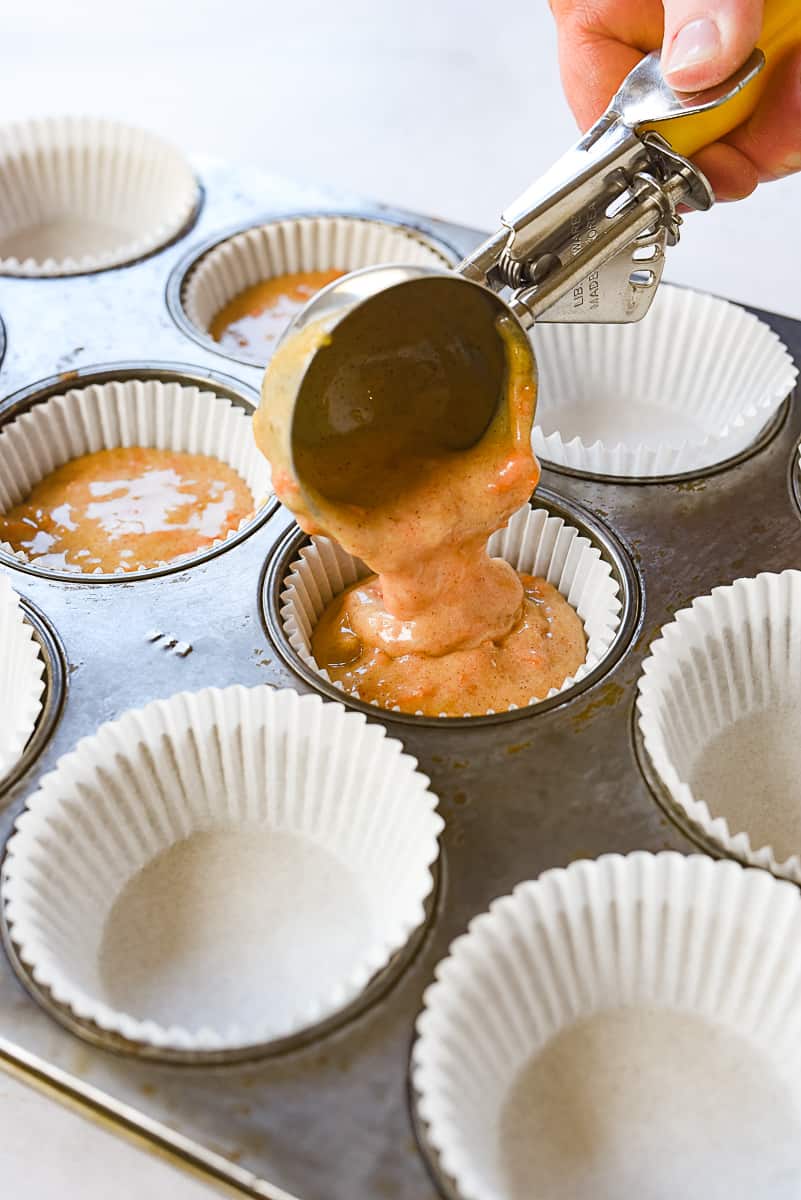 scooping carrot cupcake batter into muffin tin