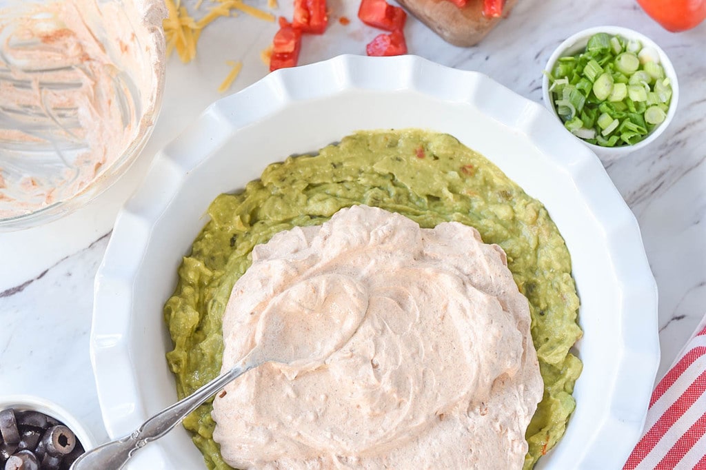 spreading sour cream over guacamole for seven layer dip