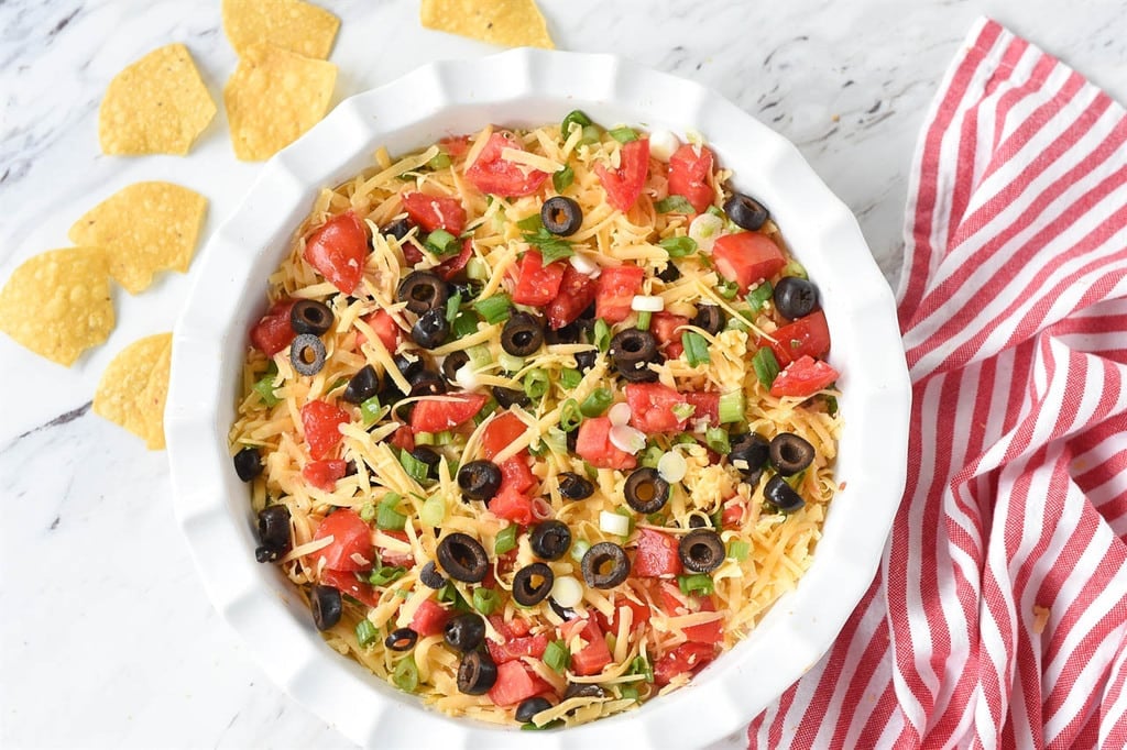 Seven Layer Dip topped with cheese tomatoes black olives and green onions