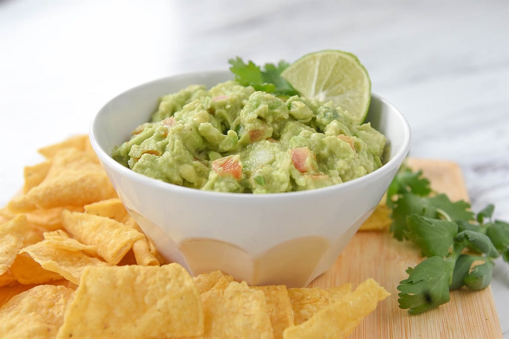 Guacamole in a bowl and chips on a board