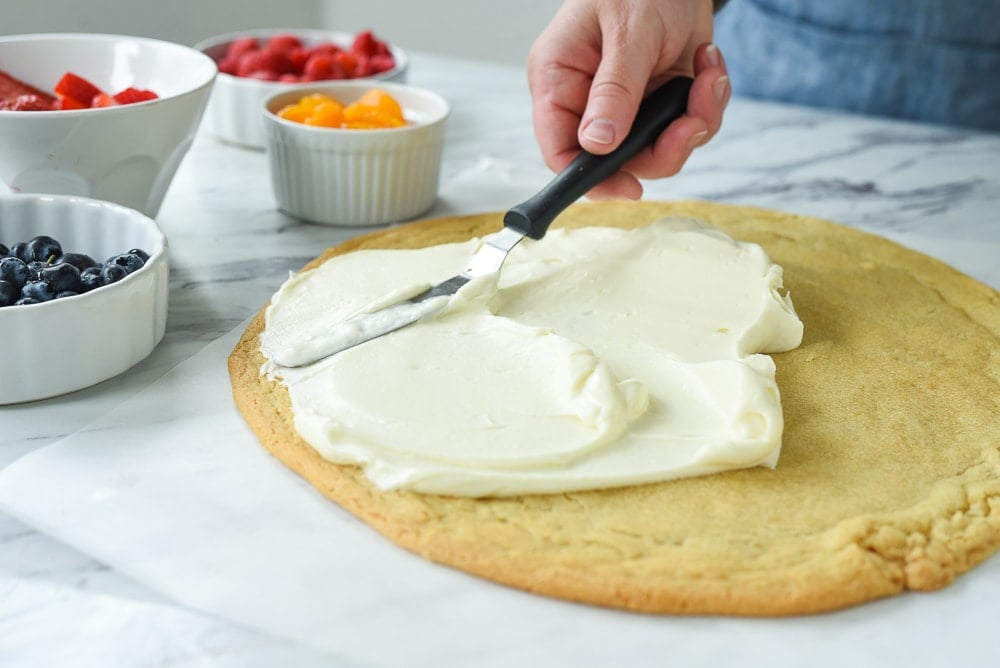 spreading cream cheese mixture on fruit pizza.