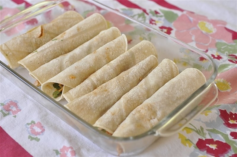 eight chicken enchiladas rolled in a glass pan