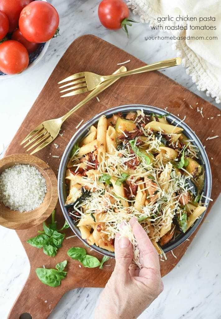 sprinkling parmesan cheese on Garlic Chicken Pasta with Roasted Tomatoes