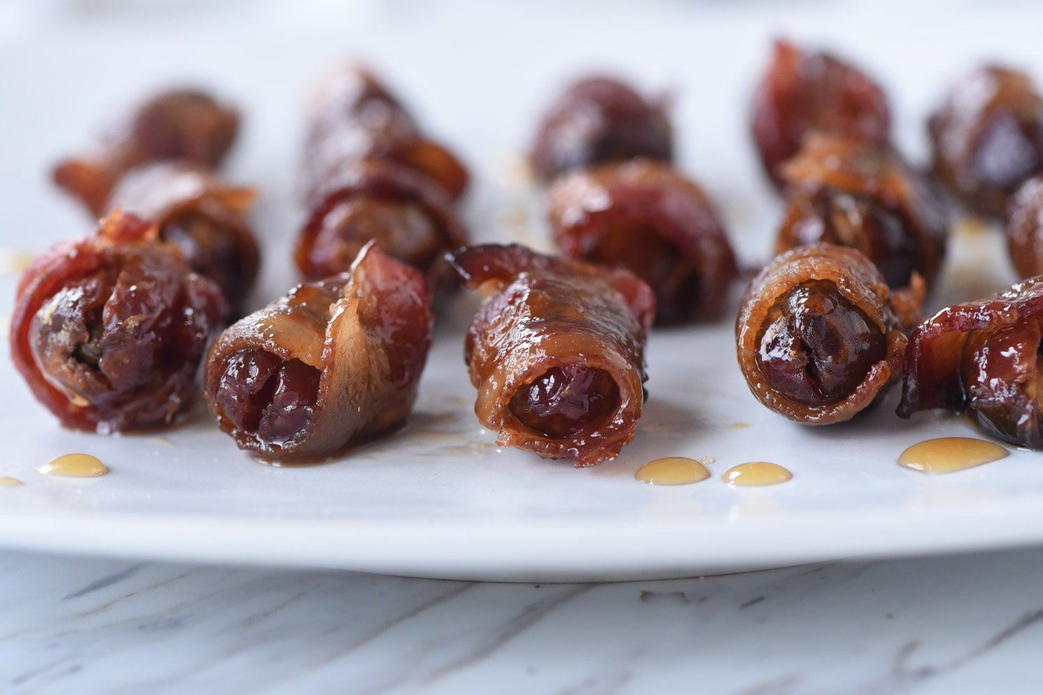 bacon wrapped dates on a white plate.