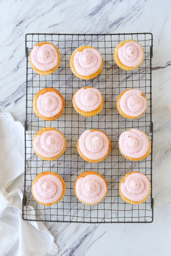 dozen pink lemonade cupcakes on a cooling rack