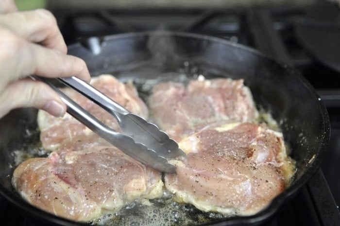 frying chicken thighs in a cast iron skillet for crispy chicken