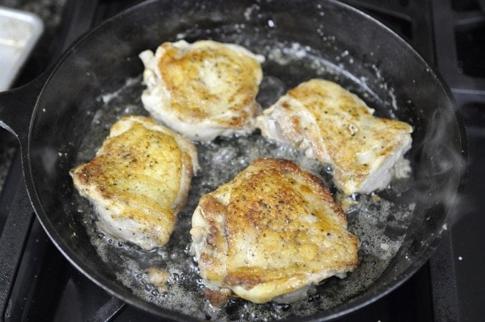 crispy chicken thighs frying in a cast iron skillet