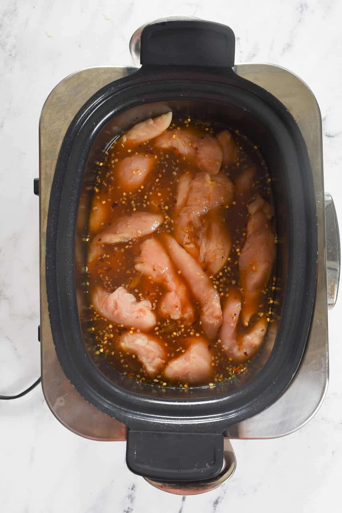 sauce poured over chicken in slow cooker