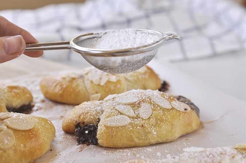 dusting Chocolate Almond Croissant with powdered sugar