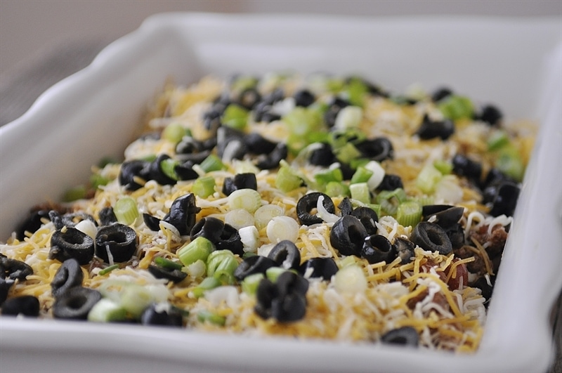 Mexican Lasagna topped with shredded cheese green onions and sliced black olives