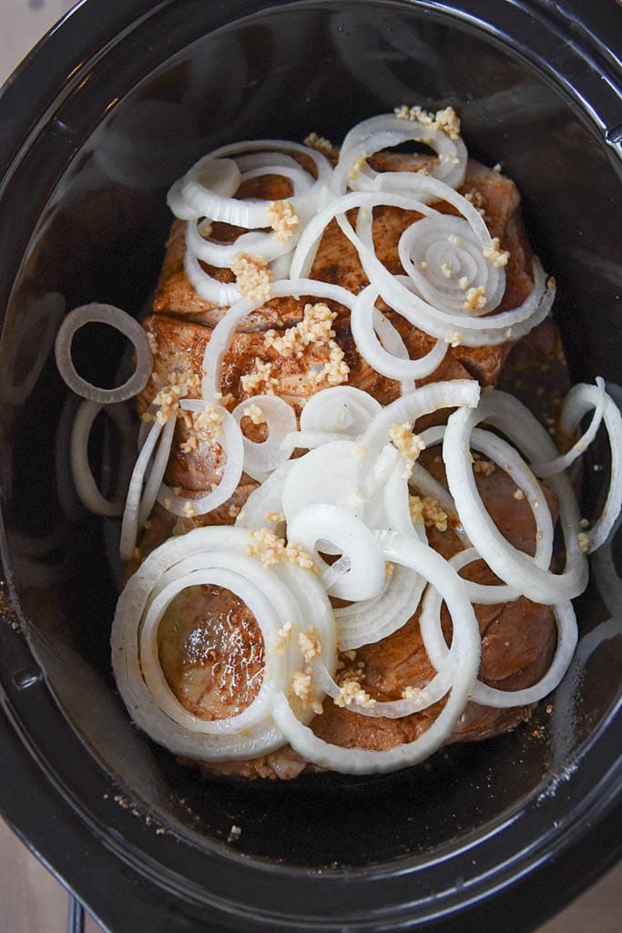 browned pork loin topped with onions in a crock pot