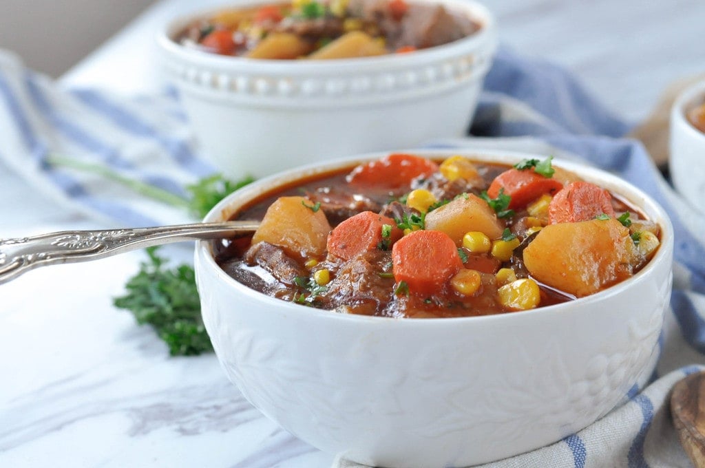 spoon in a bowl of soup with steak potatoes corn carrots