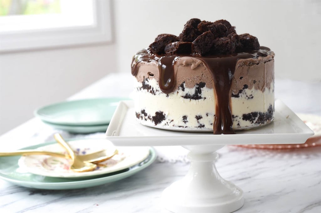 Brownie Ice Cream Cake topped with hot fudge on a cake stand