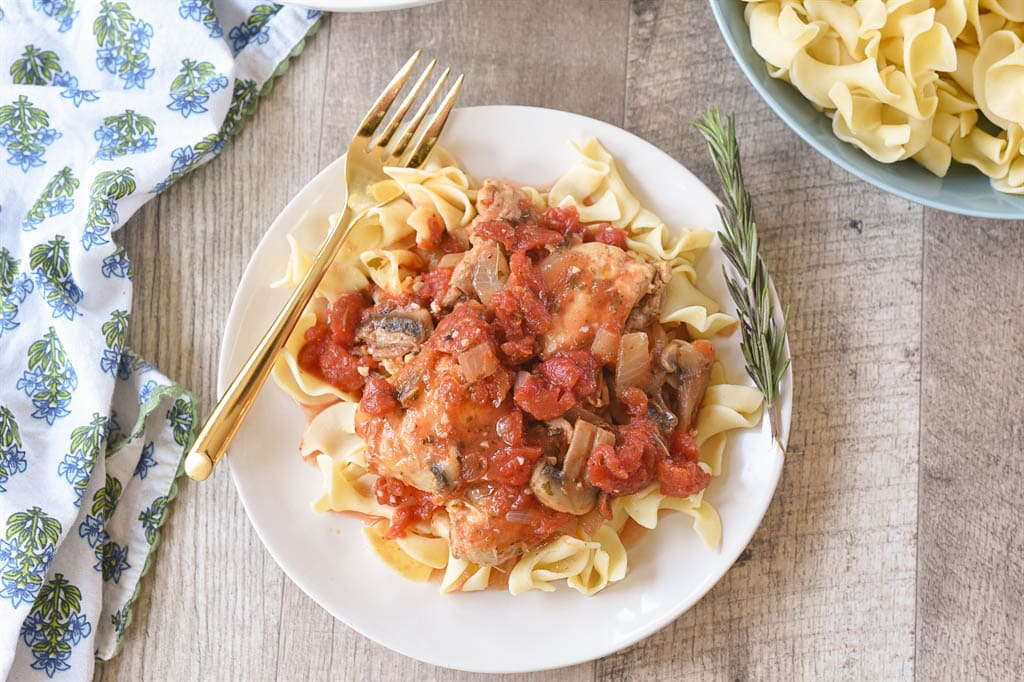 chicken cacciatore over noodles on a plate