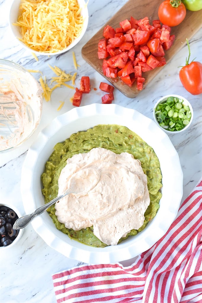 spreading sour cream over guacamole in 7 layer dip