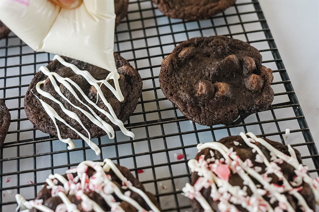 drizzling white chocolate over chocolate candy cane cookies