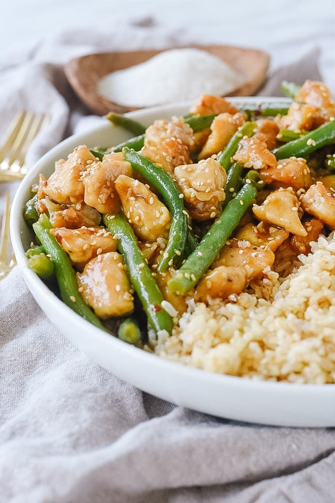white bowl of general tso's chicken with green beans and rice