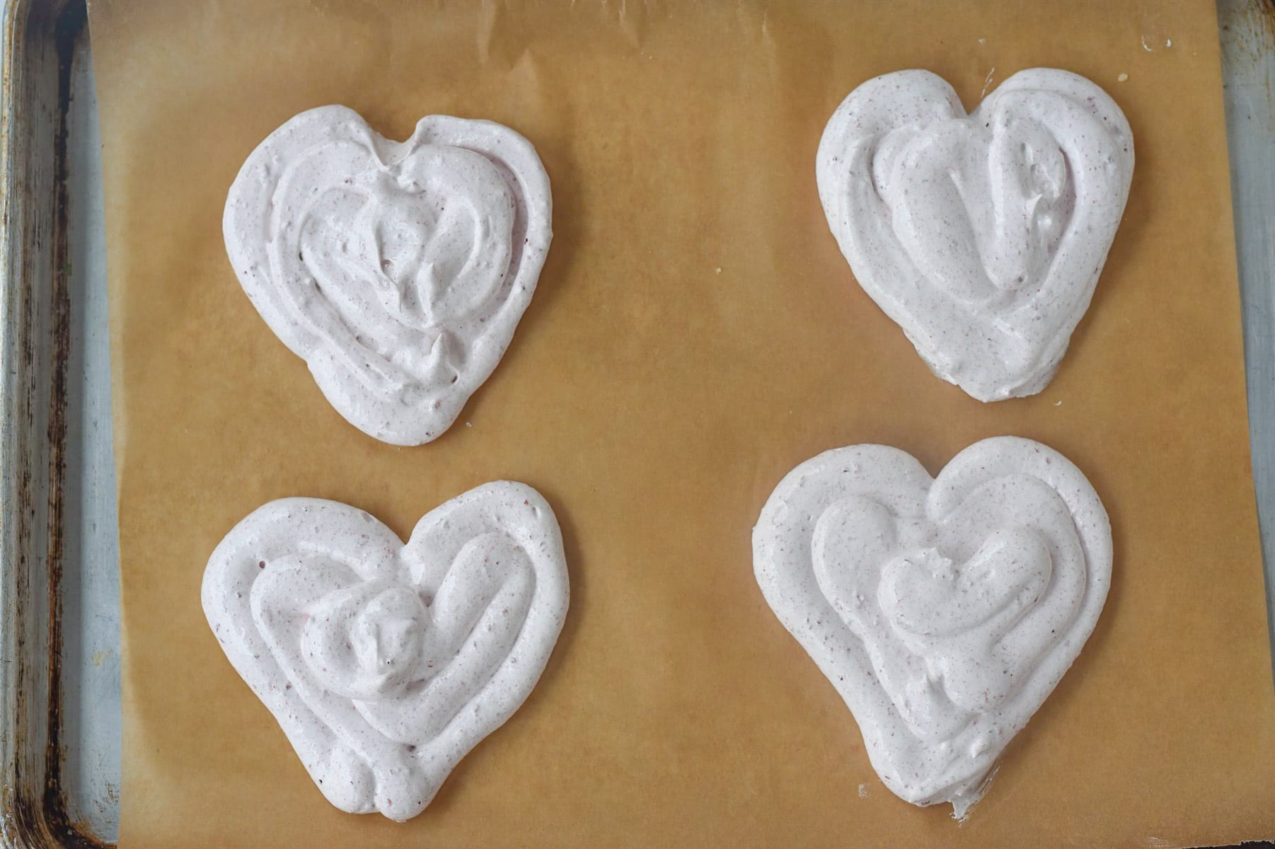four heart pavlovas on a baking sheet