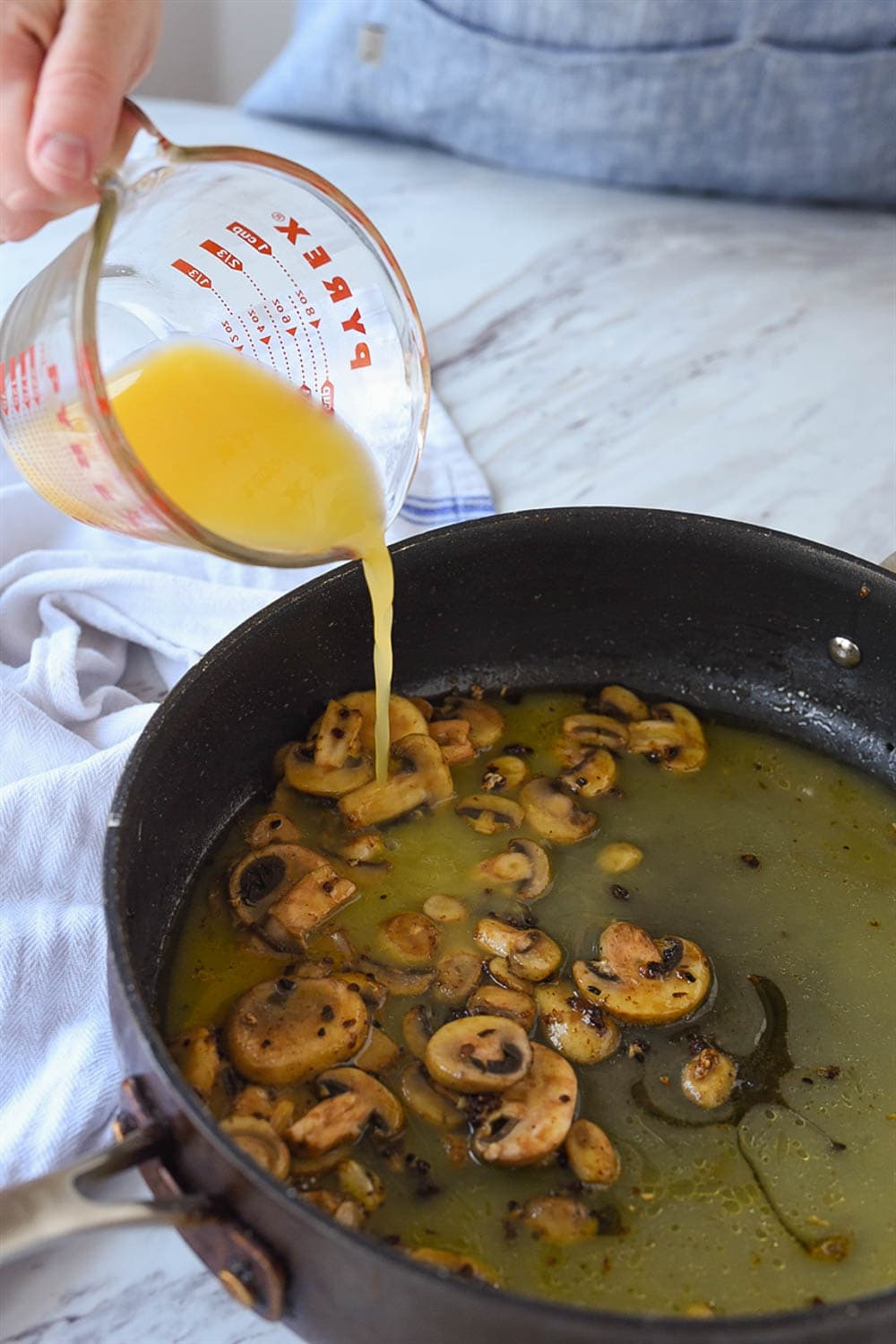 adding chicken broth to pan of mushrooms