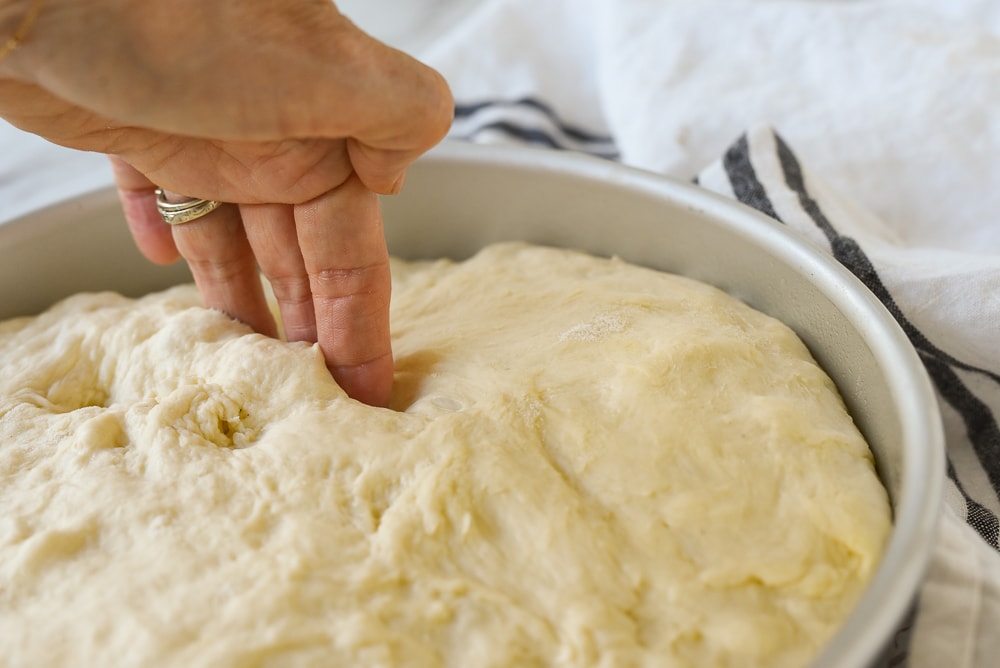 pushing fingers into focaccia bread dough