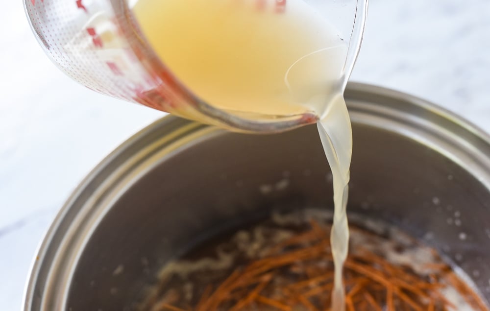 pouring chicken broth into pan