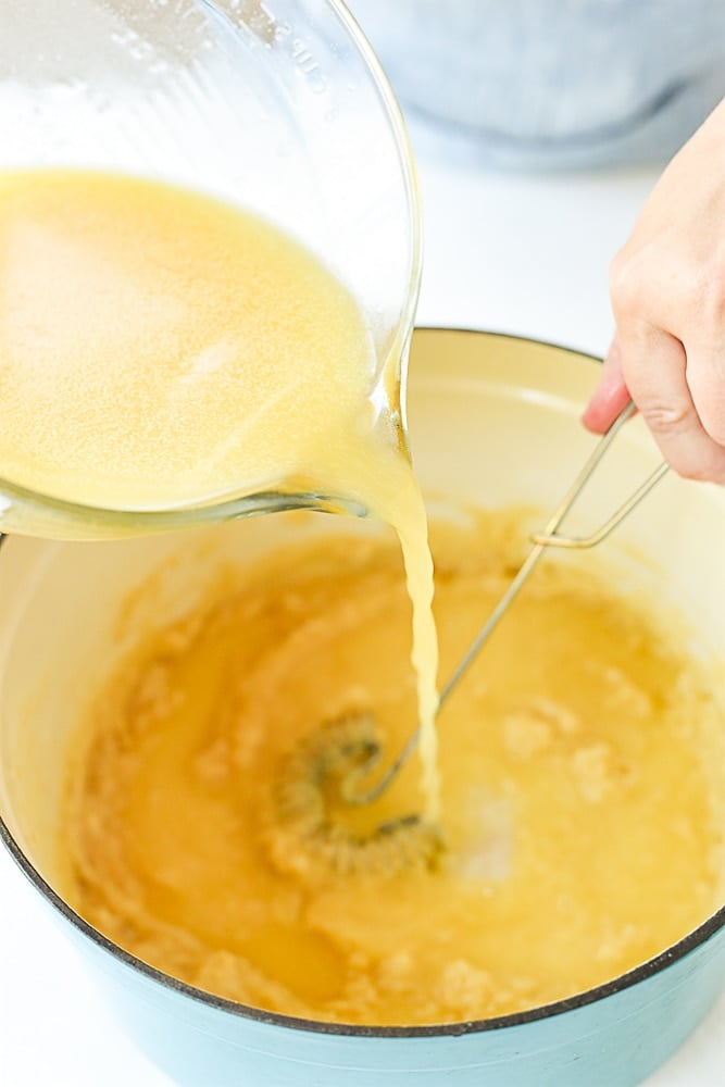 pouring chicken broth into roux