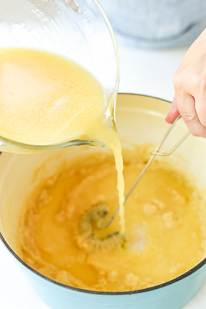 pouring chicken broth into roux