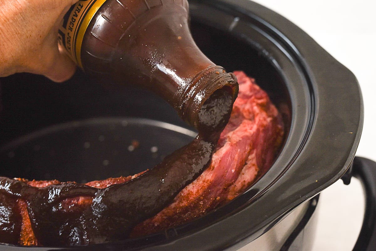 pouring BBQ sauce on crockpot ribs