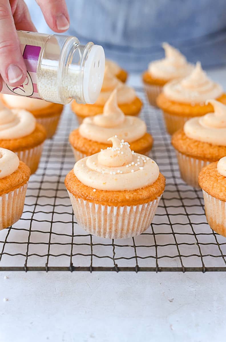 adding sprinkles to orange cupcakes