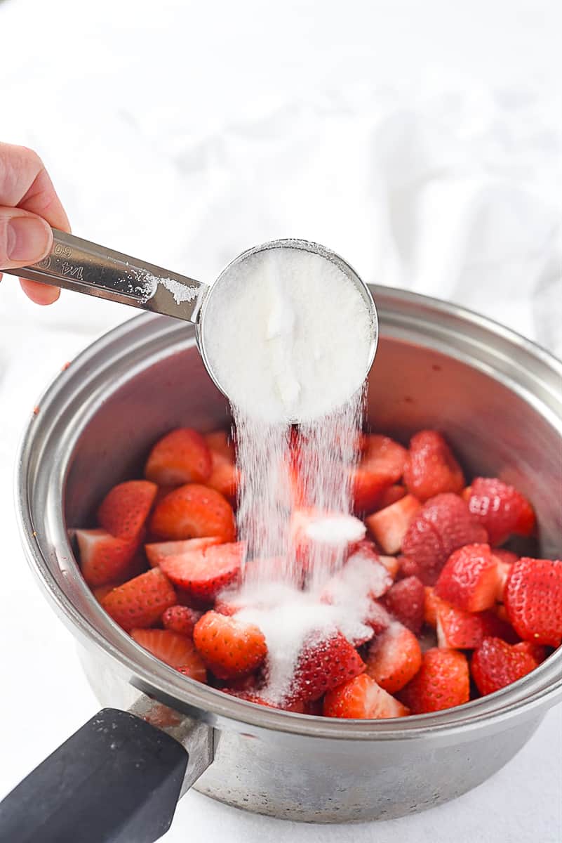 adding sugar to strawberries in a pan
