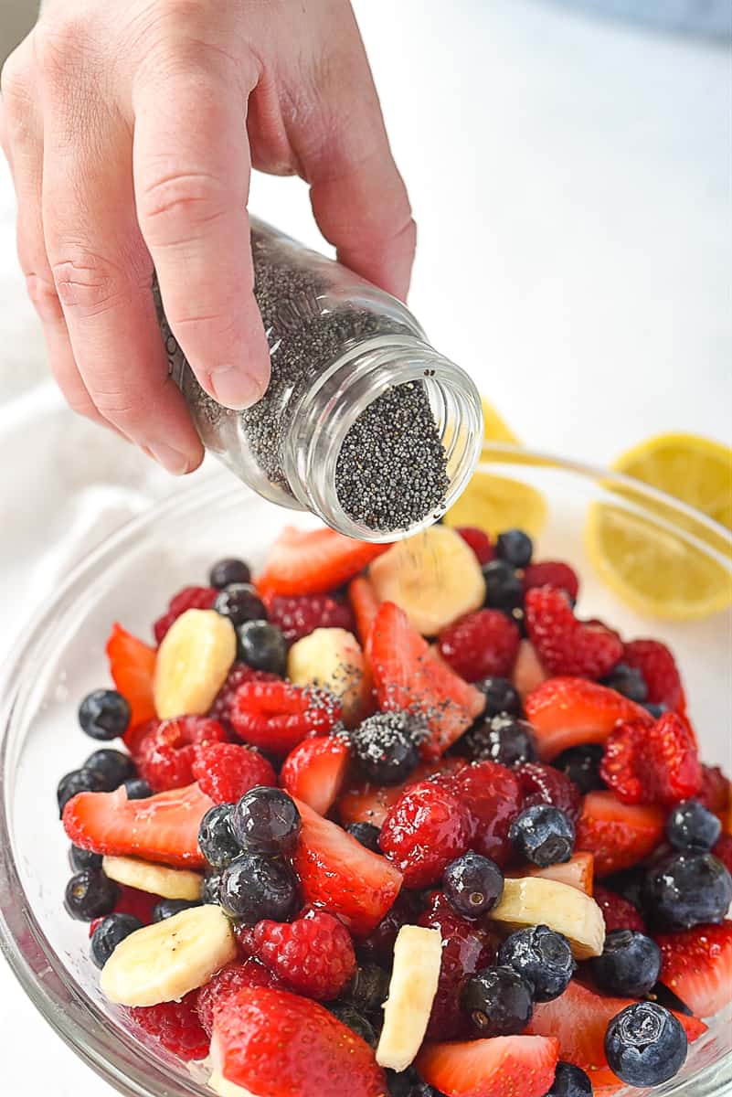 sprinkling poppy seeds on fruit salad