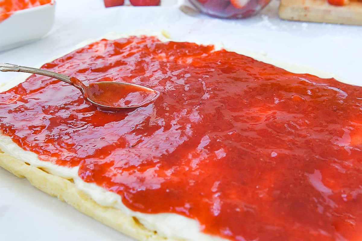 spreading strawberry glaze over cream cheese