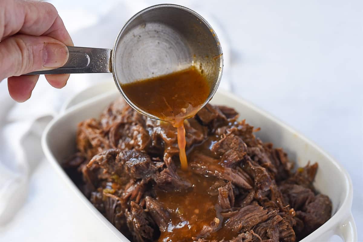 pouring gravy over beef barbacoa