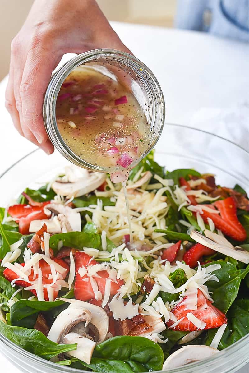 pouring dressing over spinach salad