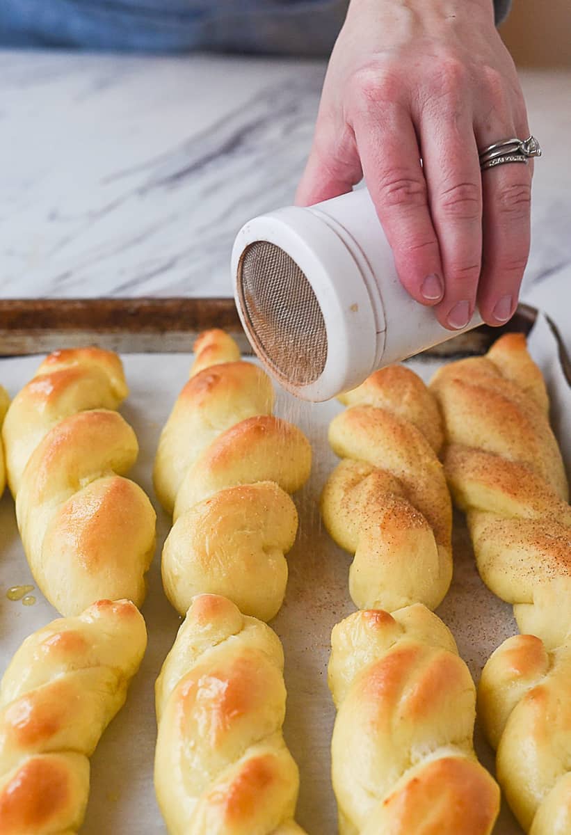 sprinkling cinnamon sugar on breadsticks