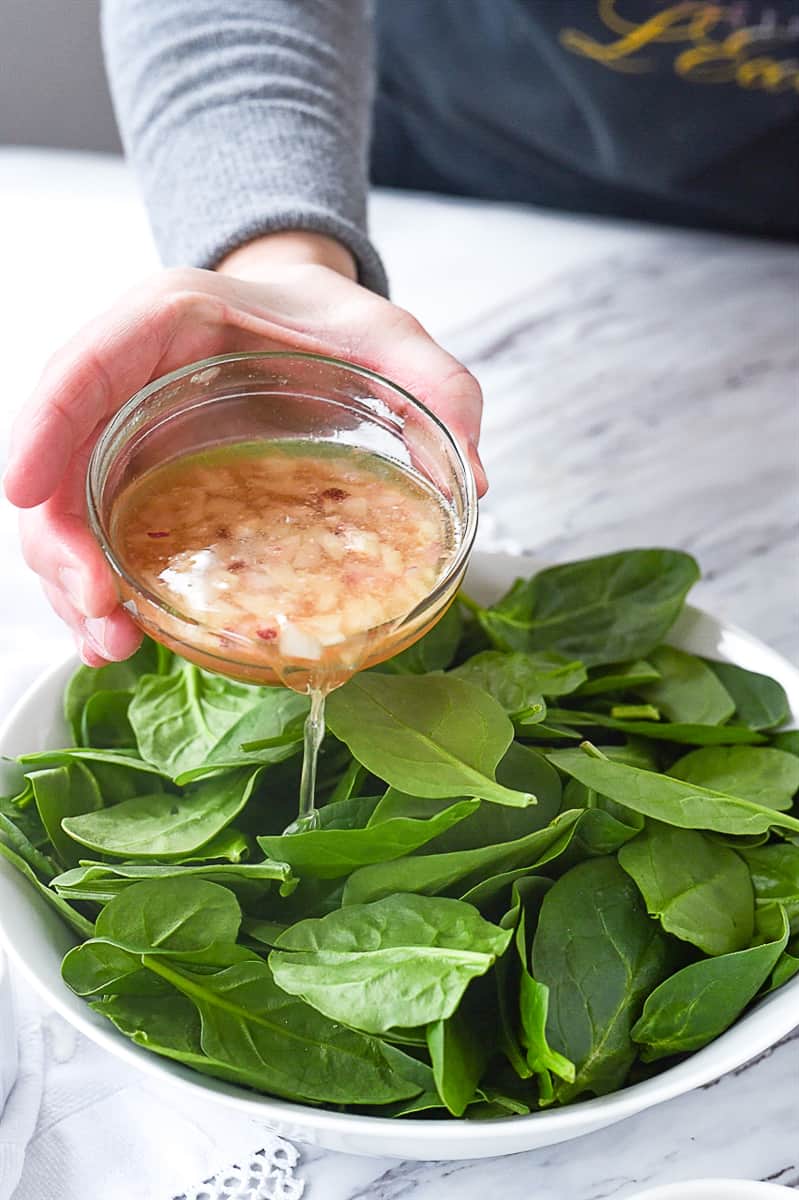 pouring vinaigrette on spinach