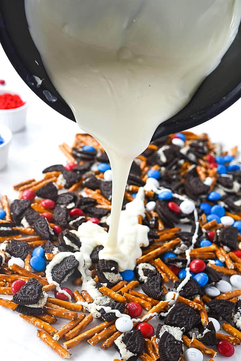 pouring chocolate over cookie bark ingredients.