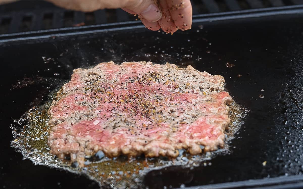 adding seasoning to smash burger