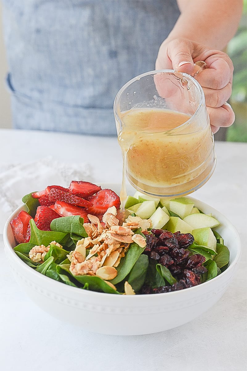 pouring dressing over spinach fruit salad