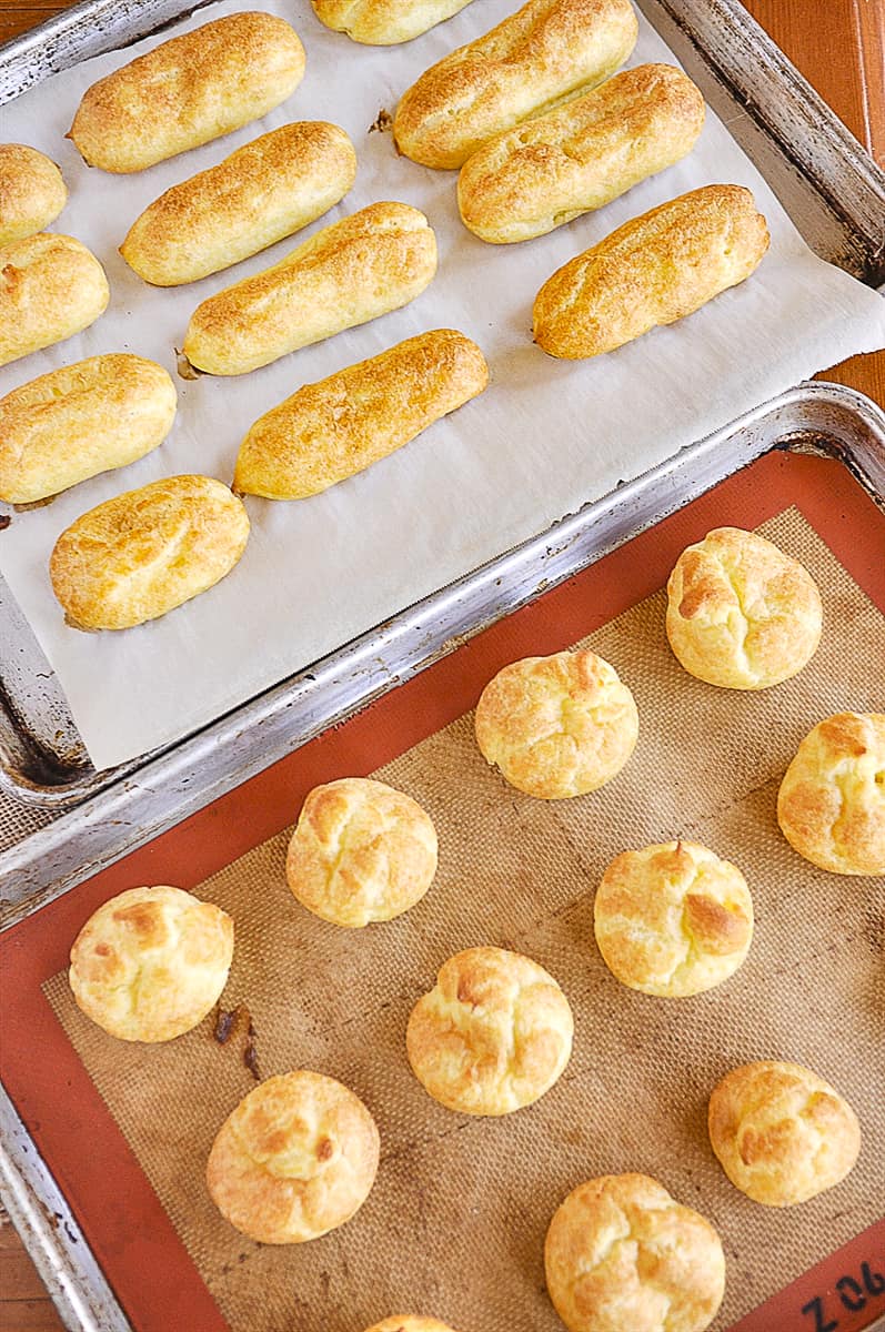 eclairs and cream puffs on a baking sheet