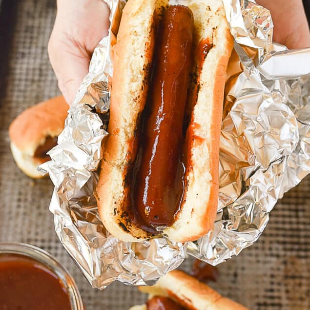 hand holding a hot dog wrapped in foil