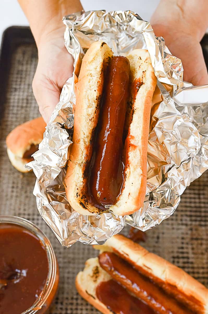 hand holding a hot dog wrapped in foil