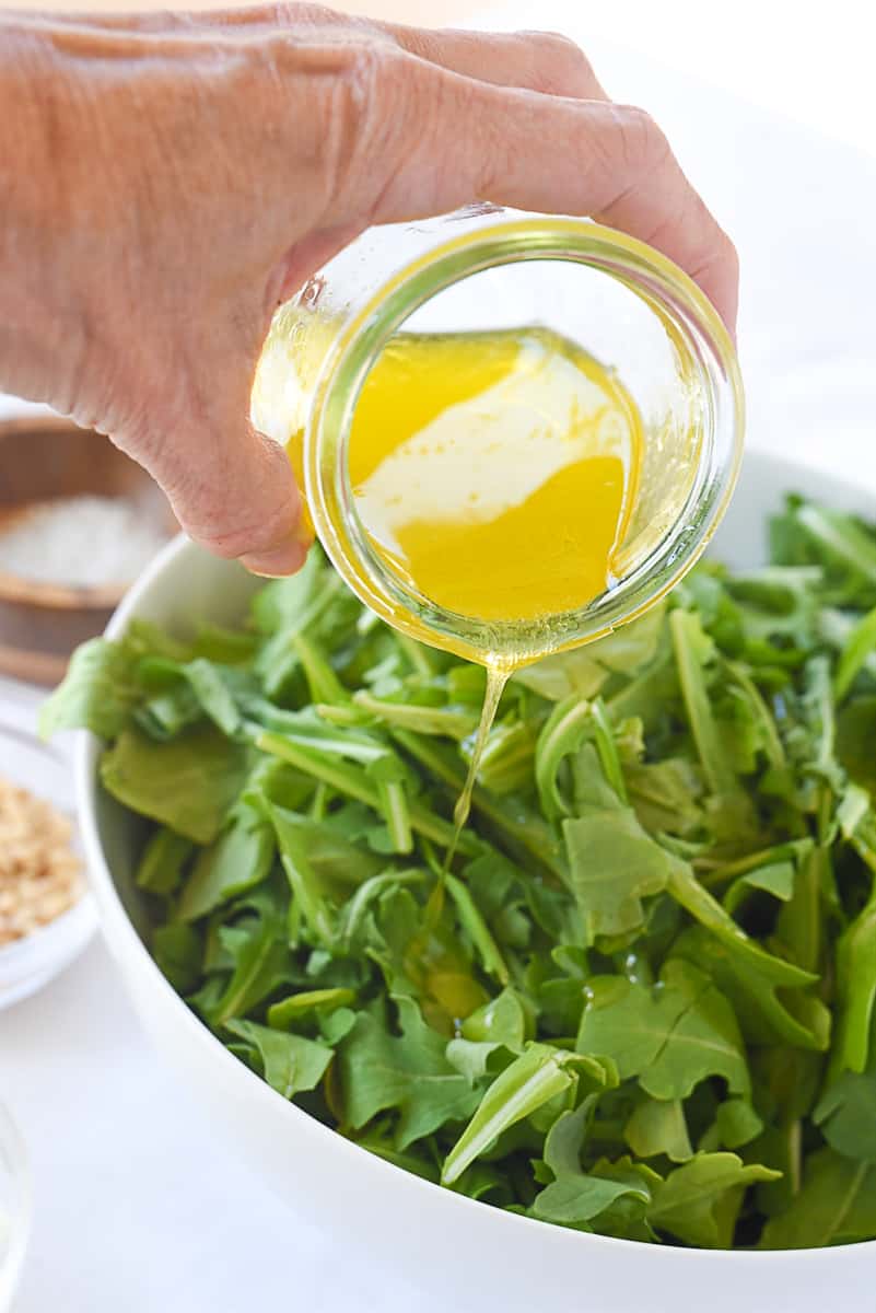 adding dressing to arugula