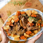 hands holding a platter full of pot roast and vegetables