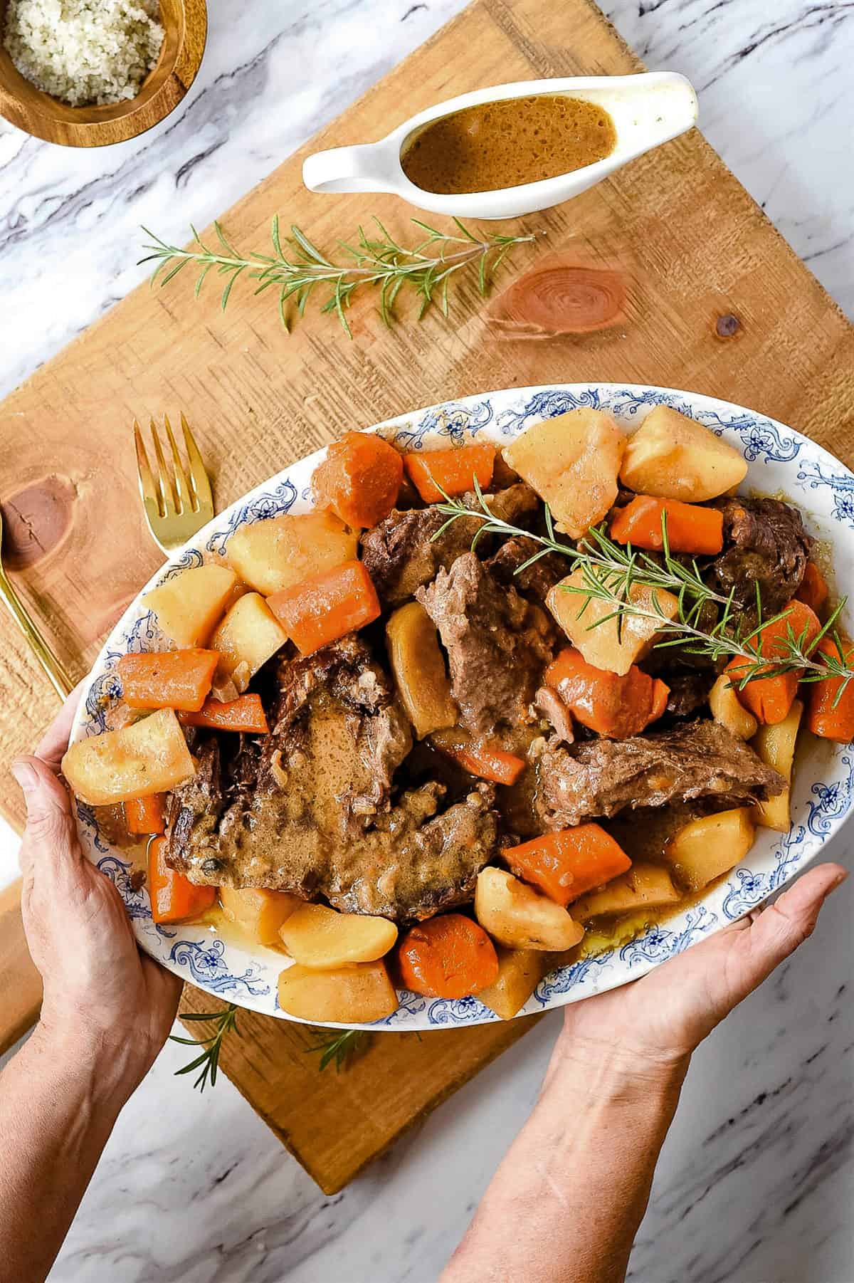 hands holding a platter full of pot roast and vegetables