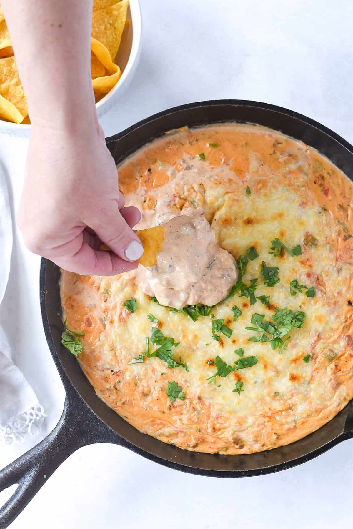 hand dipping into chili con queso in a pan