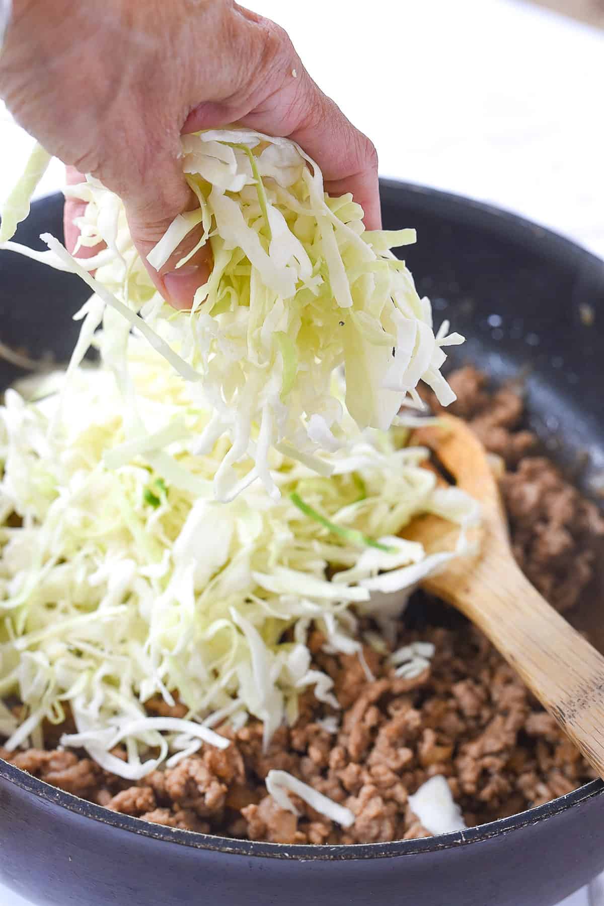 adding cabbage into frying pan