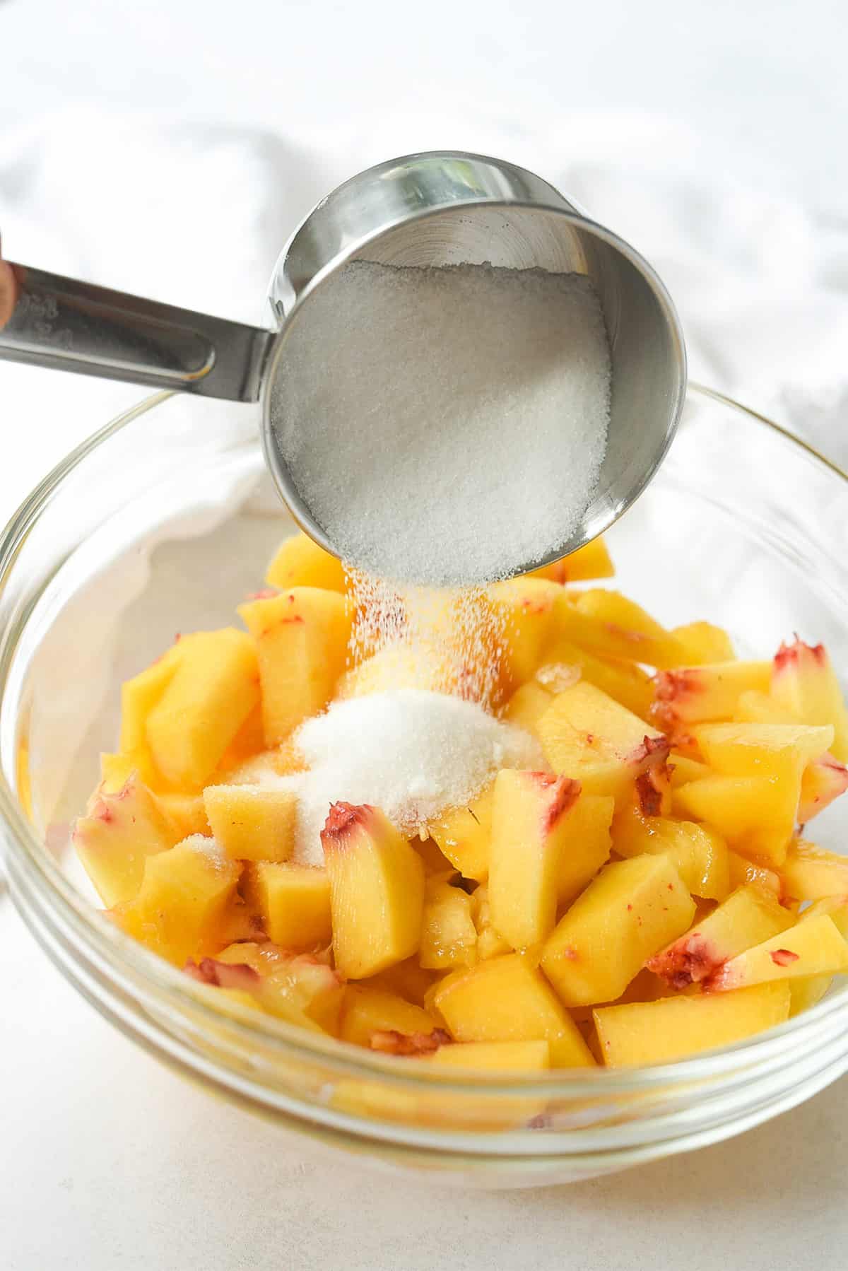 adding sugar to peaches in a bowl